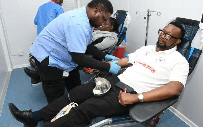 A man sits in a blood donation chair while a healthcare worker prepares to draw blood from his arm.