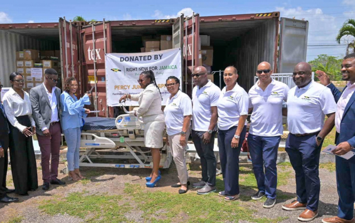 A group of representatives pose beside shipping containers filled with donated medical equipment and supplies.